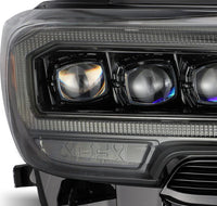 Close-up of AlphaRex NOVA-Series LED Projector Headlights in Mid-Night Black for 2016-2023 Toyota Tacoma, featuring three prominent LED projector lights encased in sleek, modern, and slightly tinted housing. The design includes bold, geometric lines and reflective surfaces, enhancing the vehicle's overall aesthetic. (SKU: 880705)