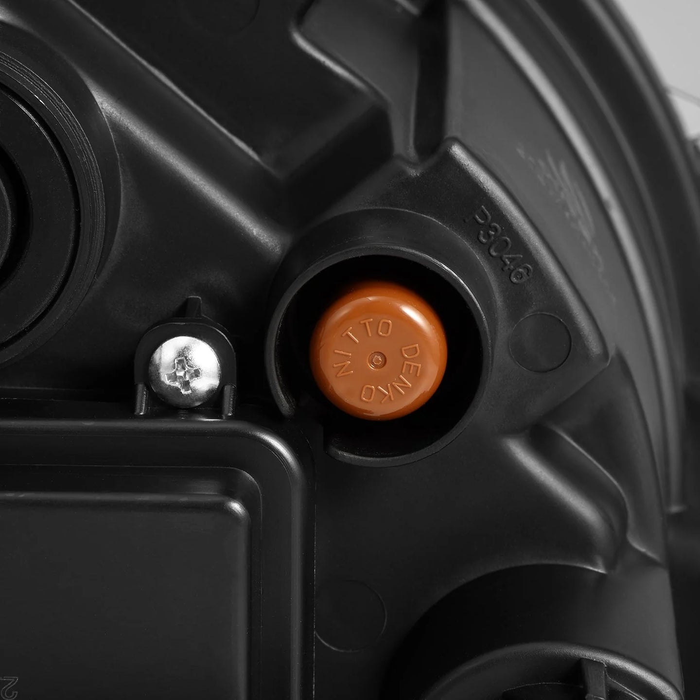 Close-up of a black mechanical device featuring various parts, including a round orange knob labeled "NITTO DENKO," a silver screw, and angular segments. Resembling the precise engineering of AlphaRex USA's AlphaRex NOVA-Series LED Projector Headlights in Black for the 2018-2023 Jeep Wrangler JL and Gladiator JT (SKU: 880868), it boasts distinct textures and markings.