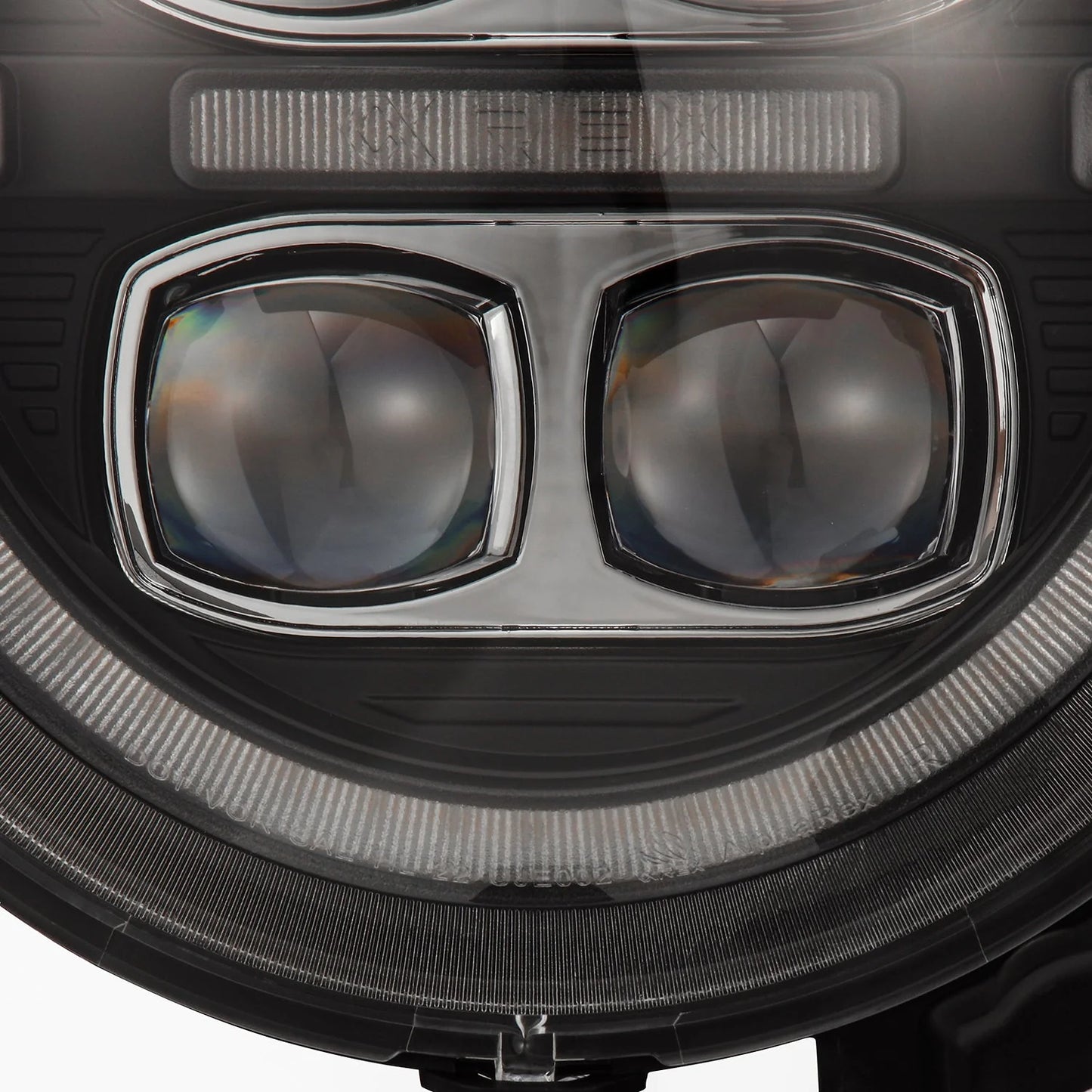 Close-up view of a Jeep Gladiator JT's LED headlight. The AlphaRex USA NOVA-Series LED Projector Headlights in Black (SKU: 880868) for the 2018-2023 Jeep Wrangler JL/Gladiator JT feature two prominent, semi-transparent lenses surrounded by concentric rings, likely representing the daytime running lights or turn signal lights. The design has a modern and sleek appearance.