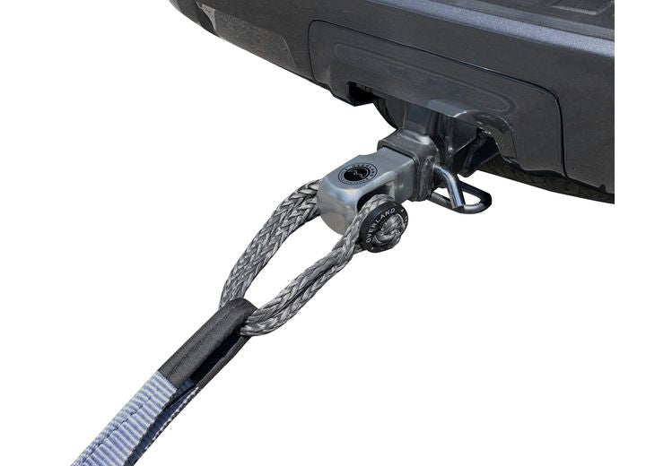 A vehicle's hitch receiver is shown with a tow strap securely attached using the Overland Vehicle Systems ALUMINUM RECEIVER MOUNT FOR SOFT SHACKLE. The strap is looped through a metal connector on the hitch, ready for secure towing purposes. The background is white, emphasizing the robust towing setup.