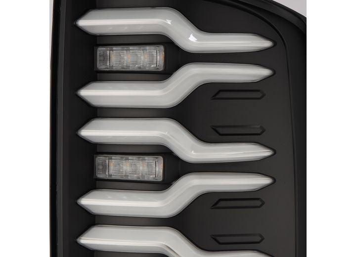 Close-up of the AlphaRex USA 14-18 SIERRA 1500/2500/3500HD LUXX LED tail lights, featuring vertically aligned, uniquely shaped LED light strips and smaller rectangular LED sections. The design incorporates a modern aesthetic with black trim surrounding the light elements, including activation lights and sequential signal functionality.