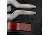 Close-up of a dark Sierra 1500/2500/3500HD's rear side, featuring distinct LUXX LED tail lights in Alpha-Black with activation lights and sequential signals from AlphaRex USA. The word "REX" is engraved on the car's body near the tail lights, with a red rectangular reflector visible below the lettering.