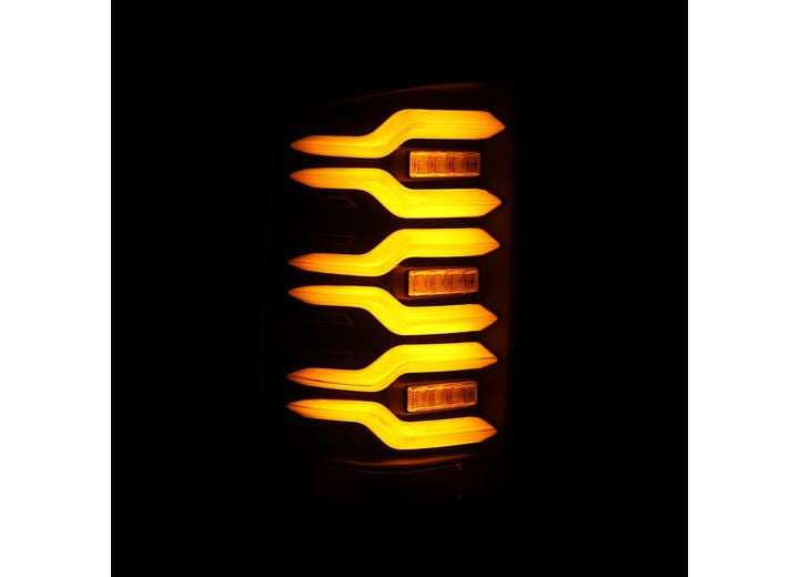 Close-up of the 14-18 SIERRA 1500/2500/3500HD LUXX LED TAIL LIGHTS ALPHA-BLACK W/ACTIVATION LIGHT & SEQ SIGNAL by AlphaRex USA, showcasing a set of yellow-orange LED lights arranged in a symmetrical pattern against a black background. The lights are glowing brilliantly, creating a futuristic and sleek design.