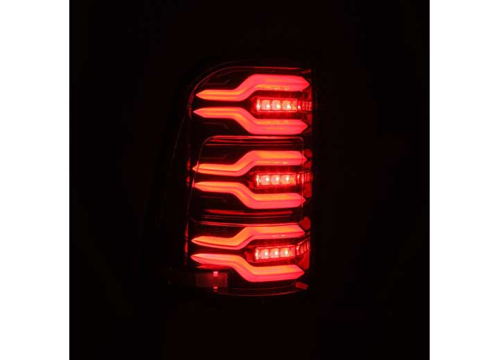 A close-up of a car's tail light illuminated in a dark setting. The AlphaRex USA RAM LUXX LED Tail Lights Alpha-Black with Sequential Signal Lights for 19-22 models feature three distinctive horizontal strips with a sleek, modern design, emitting a vibrant red glow. The curved edges of the light housing and sequential signal lights add to the stylish appearance and enhanced visibility.