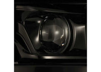 Close-up photograph of the 21-23 F150 LUXX LED Projector Headlights Alpha-Black with ACT Light & Sequential Signal by AlphaRex USA. The headlight lens reflects light, showcasing intricate details of the headlight housing. The image focuses on the circular shape of the headlight in a glossy black finish.