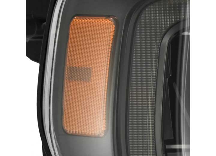 A close-up view of a vehicle's amber turn signal light, seamlessly incorporated into the 21-23 F150 LUXX LED PROJECTOR HEADLIGHTS ALPHA-BLACK W/ ACT LIGHT & SEQ SIGNAL by AlphaRex USA, with a clear protective cover. The background elements are slightly blurred, drawing attention to the rectangular orange indicator.