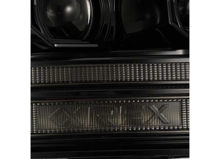 Close-up of the front grille of a black car, featuring the engraved word "CIREX." The grille boasts a textured pattern, while two round headlights—AlphaRex USA 09-18 RAM 2500 LED Projector Headlights with ACT Light, Sequential Signal, and DRL Alpha—are partially visible at the top. The entire scene radiates a sleek, reflective finish typical of polished surfaces.