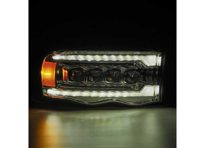 Close-up of a modern automotive headlight assembly against a dark background. The AlphaRex USA RAM 1500/2500/3500 2002-2005/2003-2005 Nova-Series LED Projector Headlights - Alpha Black feature multiple LEDs arranged in rows, with a prominent yellow-orange indicator light on the left side. The sleek design emphasizes advanced lighting technology and enhanced visibility.