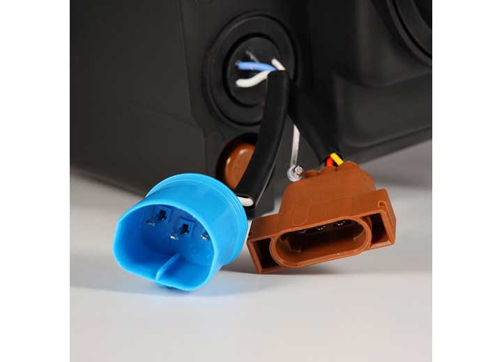 Close-up of blue and brown electrical connectors with wires attached, placed on a grey surface. These connectors appear to be part of an automotive or electronic component, possibly for linking AlphaRex USA's RAM 1500/2500/3500 2002-2005/2003-2005 Nova-Series LED Projector Headlights in Alpha Black for enhanced visibility. The background is slightly blurred.