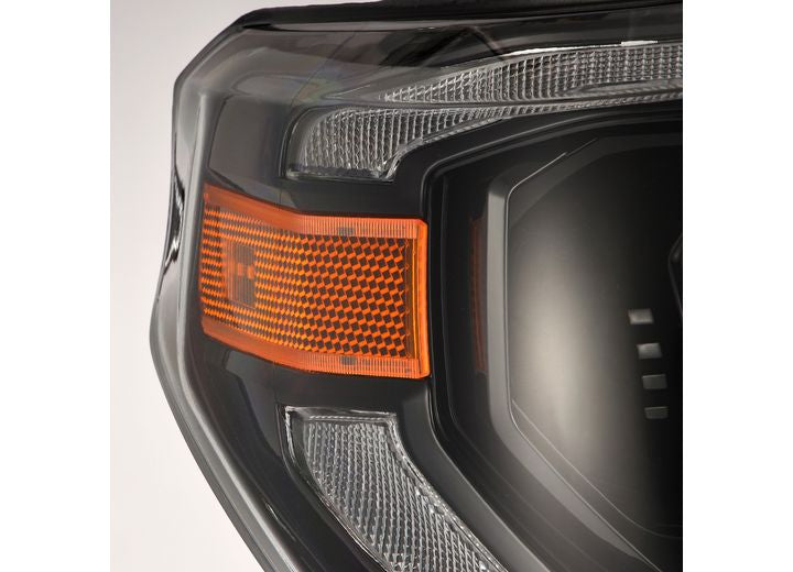 Close-up of the Tundra 14-21 LED Projector Headlights with Sequential Signal & DRL by AlphaRex USA, featuring modern design elements. The headlights include a prominent orange indicator light and intricate details showcasing reflective surfaces, geometric patterns, and sequential signals.