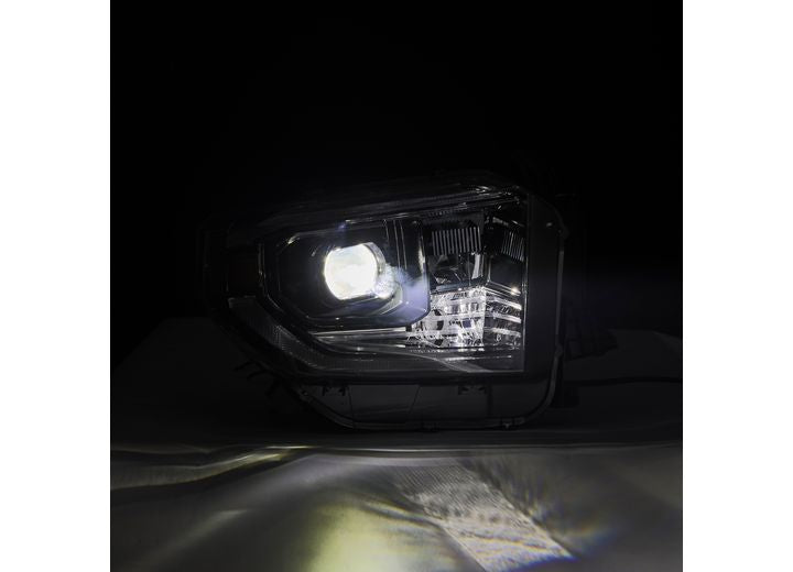 Close-up of the Tundra 14-21 LED Projector Headlights with Sequential Signal & DRL by AlphaRex USA against a dark background. The headlight emits a bright beam of light, illuminating the surface in front of it.