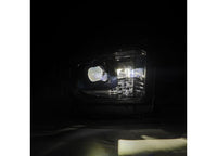 Close-up view of the Tundra 14-21 LED Projector Headlights with Sequential Signal & DRL by AlphaRex USA illuminated in a dark setting. The LED headlights emit a bright beam, highlighting the details of the headlight's reflective and refractive components. The surrounding area is shrouded in darkness.