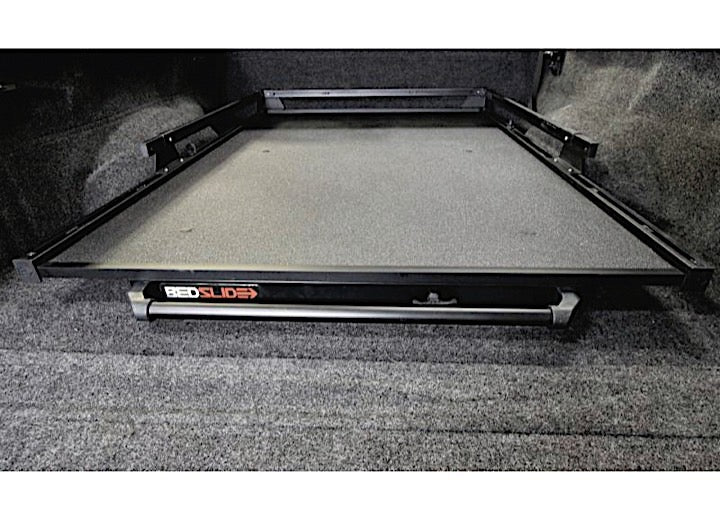 A truck bed featuring a Bedslide BEDSLIDE 1500 CONTRACTOR BLACK 68IN X 48IN, fully extended. The sliding cargo platform has a flat, gray surface within a black metal frame, designed for easy access. The truck bed is lined with dark gray carpet material, showcasing its durable construction.