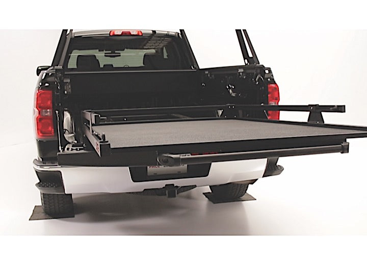 A black pickup truck with its tailgate down reveals a Bedslide 73IN x 48IN BEDSLIDE MAX EXTENSION 1500 - BLACK extended outward. The extension, designed for easy loading and access, appears sturdy and is lined with a textured material. The background is a plain white studio setting.