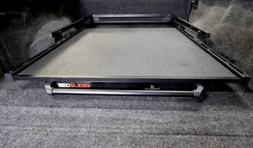 The BEDSLIDE 1000 CLASSIC BLACK 63IN X 47IN by Bedslide is a heavy-duty cargo slide designed for installation inside a vehicle's trunk. It features a flat, textured surface and black frame with the "RED SLIDE" logo. Specifically designed to handle heavy loads and enhance truck bed functionality, it ensures easy loading and unloading of items.