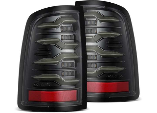 A pair of AlphaRex USA 11-18 RAM LUXX LED Tail Lights in Alpha Black featuring modern, angular designs. They include horizontal LED light strips and a prominent red reflector on the lower section. The brand name "AlphaRex" is subtly visible on the bottom part of each taillight, complete with sequential signal functionality and activation light.