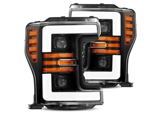 A pair of sleek, black 17-19 F250/F350/F450/F550 Super Duty Pro-Series Projector Headlights by AlphaRex USA, featuring white L-shaped LED daytime running lights and amber turn signals embedded within. The clear lenses showcase the intricate detailing of the internal components.