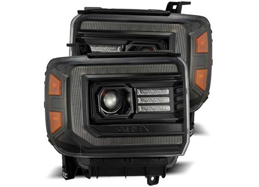 A set of AlphaRex USA 14-18 Sierra Luxx-Series LED Projector Headlights in Alpha-Black, showcasing a black rectangular design with LED strip accents, orange side markers, and projector beam lenses, positioned one slightly in front of the other against a white background for enhanced visibility.