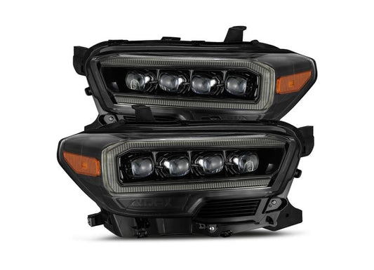 Image of two AlphaRex NOVA-Series LED Projector Headlights with a modern, sleek design. These mid-night black headlights by AlphaRex USA for the 2016-2023 Toyota Tacoma feature multiple individual bulbs encased in a dark housing with reflective elements. Amber side markers are visible on the edges, and the overall look is futuristic and stylish, fully embracing AlphaRex NOVA-Series aesthetics (SKU: 880705).