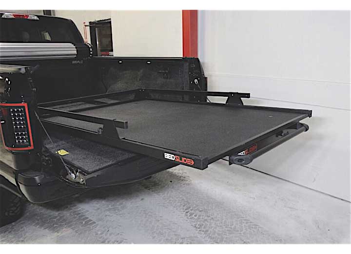 A truck bed featuring the Bedslide BEDSLIDE 1000 BLACK 65IN X 48IN heavy-duty slide-out platform is shown fully extended. This tray ensures easy access and organization of the truck bed's contents. The interior of the truck bed appears clean, with a portion of the tailgate visible on the left side.