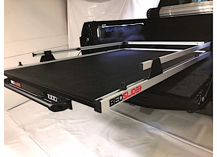 A photo showing a truck bed slide-out accessory, branded as "BEDSLIDE 1000 CLASSIC 70IN X 41IN" from Bedslide, installed in a truck. The sliding drawer system is extended out from the truck bed, featuring a black surface and aluminum rails with heavy-duty construction, making it easier to access cargo without climbing into the truck bed.